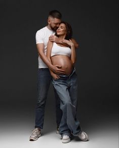 a pregnant man and woman standing next to each other in front of a dark background