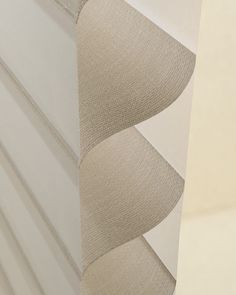 the corner of a wall with white and beige fabric on it's side, next to a window