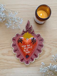 a heart shaped paper cutout sitting on top of a wooden table next to a candle