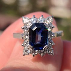 a close up of a person's hand holding a ring with an oval shaped blue and white diamond