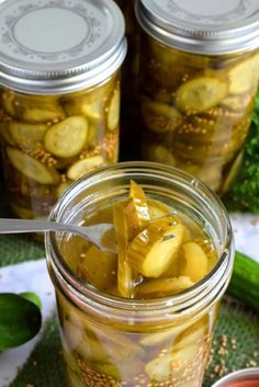 pickled cucumbers in jars with spoons on the table next to them