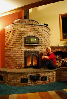 a woman sitting on the floor in front of a brick oven with wood burning inside