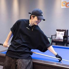 a man in black shirt and hat holding pool cues near pool table with blue cloth on it