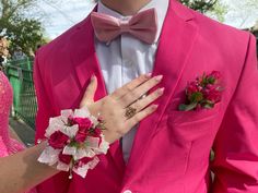 a man in a pink suit and flower boutonniere with his hand on the woman's lapel