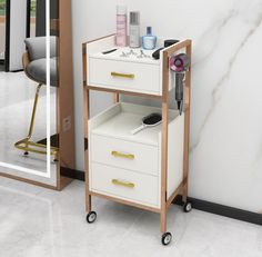 a white and gold cart with two drawers next to a mirror on the floor in front of a marble wall