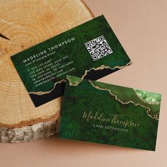 two green business cards sitting on top of a tree stump next to a piece of wood