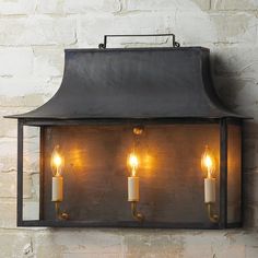 three candles are lit in an old fashioned light fixture against a brick wall with exposed lighting