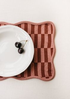 two cherries are sitting on a plate with a checkered placemat behind it