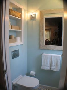 a white toilet sitting in a bathroom next to a wall mounted shelf with towels on it