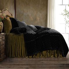 a bed with black and gold comforters in a room next to a window,