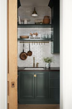 a kitchen with green cabinets and white brick backsplash, open shelving above the sink