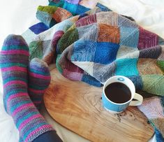 a cup of coffee and some colorful socks on a wooden board with a blanket over it