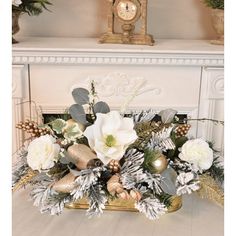 a christmas centerpiece with white flowers and greenery in front of a fireplace mantel