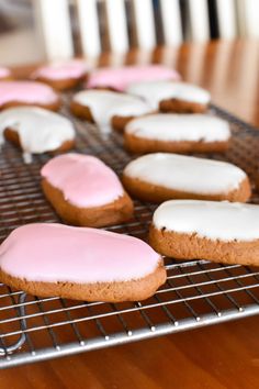 pink and white frosted cookies cooling on a wire rack in a kitchen area with wooden flooring