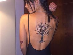 a woman with a tree tattoo on her back is standing in front of a mirror