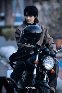 a man sitting on top of a motorcycle wearing a black jacket and helmet with his hand on the handlebars