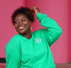 a woman in a green shirt is smiling and holding her hair up with one hand