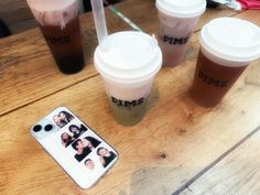 three coffee cups sitting on top of a wooden table next to a cell phone case