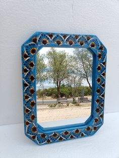 a blue and yellow mirror sitting on top of a white wall next to a tree