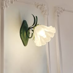 a light that is on the side of a white wall with a flower in it