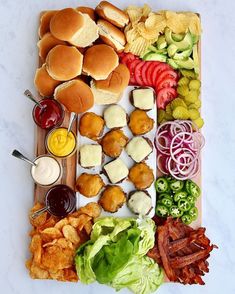 an assortment of food is laid out on a cutting board, including burgers, lettuce, tomatoes, and other foods