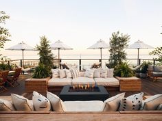 an outdoor seating area with couches, tables and umbrellas over looking the ocean