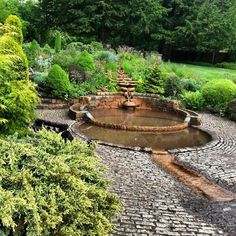 an outdoor fountain surrounded by greenery and cobblestone walkways in a garden