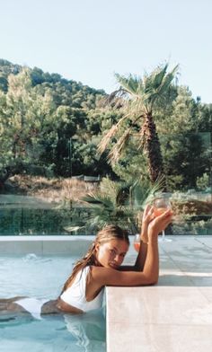 a woman sitting in a pool holding a glass with water and palm tree behind her