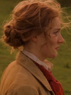 a woman standing in the grass with her hair blowing in the wind and looking off into the distance