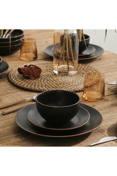 a wooden table topped with black plates and bowls