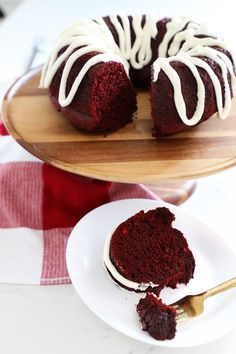 a red velvet bundt cake with white icing on a wooden platter next to a fork