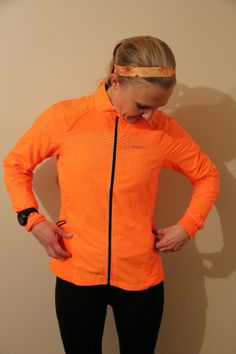 a woman wearing an orange jacket and black leggings standing in front of a wall