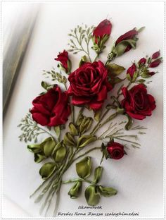 some red roses are laying on a white surface with a knife in the middle and green stems sticking out of it