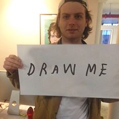 a man holding up a sign that says draw me