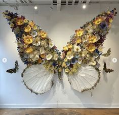 an arrangement of flowers and butterflies on display in a room with white walls, wooden flooring