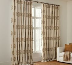 a living room with a white couch and large window covered in beige curtaining next to a chair