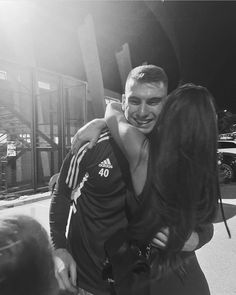 a man and woman hug each other outside in front of a building while the sun shines on them