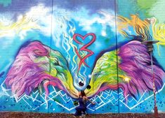 a woman is standing in front of a wall painted with two colorful birds and the word love