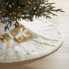 a christmas tree with presents under it on a white rug next to a lit up christmas tree