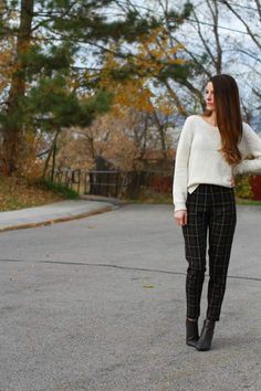 a woman standing in the street wearing black and white checkered pants, a cream sweater and black ankle high boots