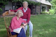 an older couple sitting on a rocking chair in front of a house