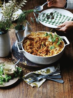 a person is serving food from a casserole dish on a wooden table with plates and utensils