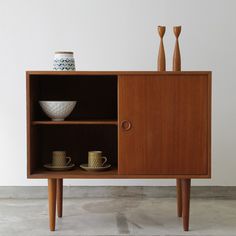 a wooden cabinet with two cups and saucers on it's sides, sitting against a white wall