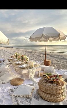 a table set up on the beach with an umbrella over it and other food items