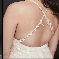 the back of a woman's wedding dress with white flowers and leaves on it