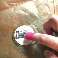 a finger is pointing at a button on a piece of brown paper with a hand drawn on it