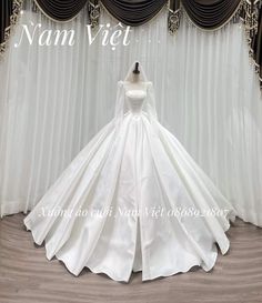 a white wedding dress on display in front of curtains with the name namvijet