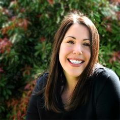 a woman smiling in front of some bushes