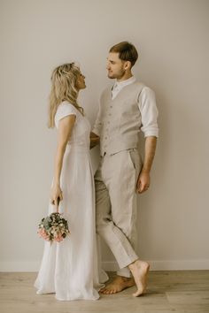 a man and woman standing next to each other in front of a wall holding flowers