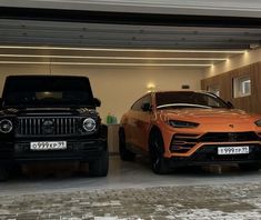 two cars are parked in a garage with lights on and one has an orange car